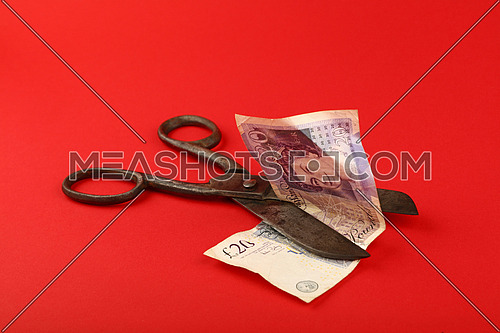 UK and Great Britain financial crisis, decline of British economy and pound illustrated, old vintage scissors cut twenty pounds banknote over red