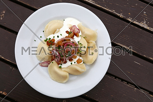 Plate of pierogi or varenyky stuffed filled dumplings with sour cream, bacon and onion, traditional East Europe cuisine meal popular in Poland, Ukraine, Slovakia and Russia, close up, elevated top view