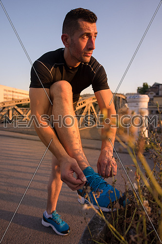 man tying running shoes laces getting ready to run on city at sunny morning