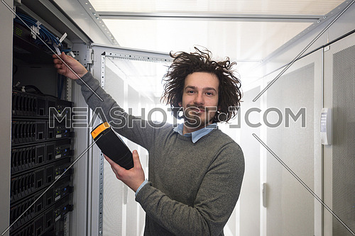 young IT technician using digital cable analyzer on server in large data center