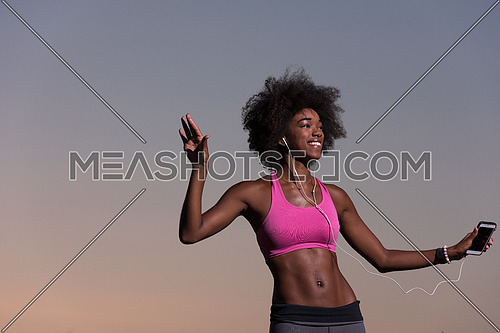 Young beautiful black girl laughs and dances outdoors with a mobile phone in her hands in a meadow beautiful summer night