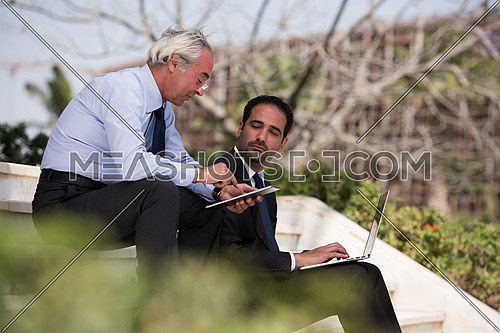 Business executives sitting on stairs of a corporate building discussing business and working online with tablet