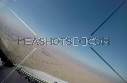Close shot from inside plane cockpit showing sky horizon from the window and desert at day