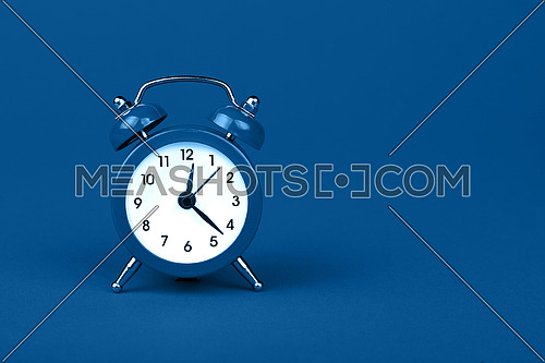 Close up one small blue metal twin bell retro classic alarm clock over blue paper background with copy space, low angle front view
