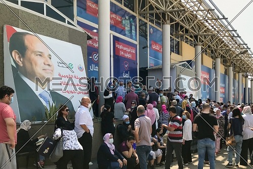 Cairo, Egypt - August 14 2021: Egyptian citizens at Exhibition land waiting for their turn to receive the Covid-19 coronavirus vaccine, with background of big photo of President Abd El Fattah El Sisi