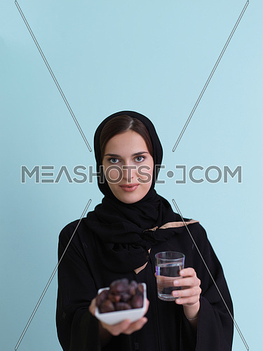 Modern muslim woman in abaya holding a date fruit and glass of water in front of her. Concept celebration of iftar time, end of fasting, in ramadan holy month