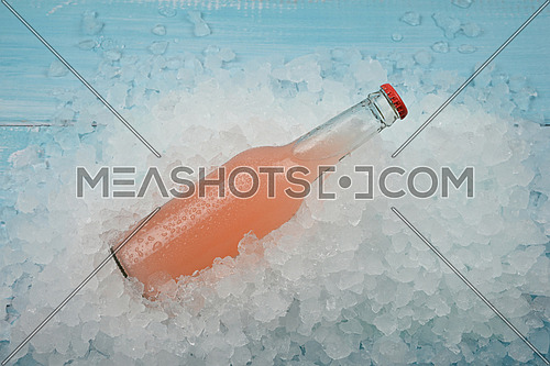 Close up one glass bottle of cold pink grapefruit cocktail on crushed ice at retail display, high angle view