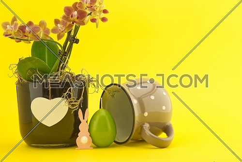 Easter Decoration with flowers, egg shaped candle and Easter Rabbit figure over a yellow background. Happy Easter card concept with free copy space for text
