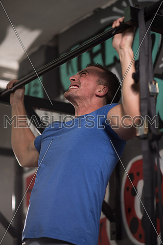 strong young man doing pull ups on a bar in a gym