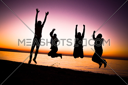 four friends jumping at the beach by sunset magic hour
