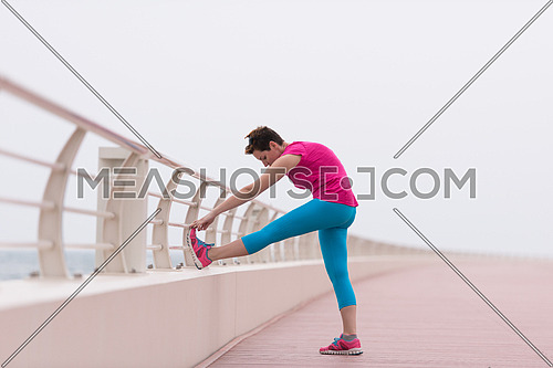 very active young beautiful woman stretching and warming up on the promenade along the ocean side to keep up her fitness levels as much as possible