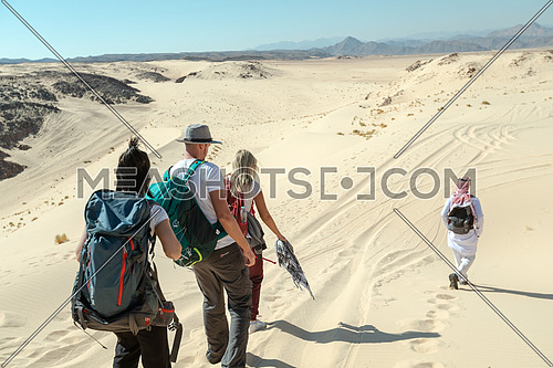 Long shot for group of tourists walking on sands with bedouin guide while exploring Sinai Trail from Ain Hodouda by day.