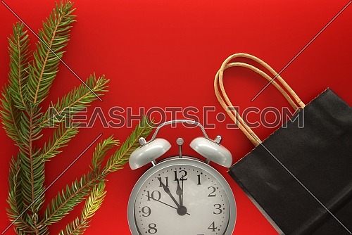 Black paper shopping bag, alarm clock and fir branch on red background with copy space for text. Black Friday sale, shopping concept