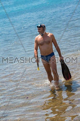 Young smiling fisherman with equipment standing in the shallow water of the sea while preparing for underwater fishing  active holiday concept