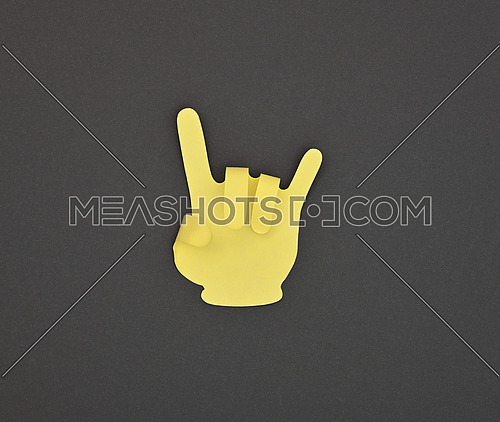 Paper made yellow DEVIL HORNS hand gesture sticker over grey background