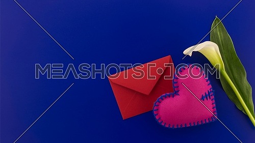 Red envelope, felt heart and white arum lily over a festive blue background with free copy space. Wishes, greetings and love message