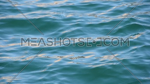 Close up background of blue sea waves and ripples with bright flare sparkles running on water surface