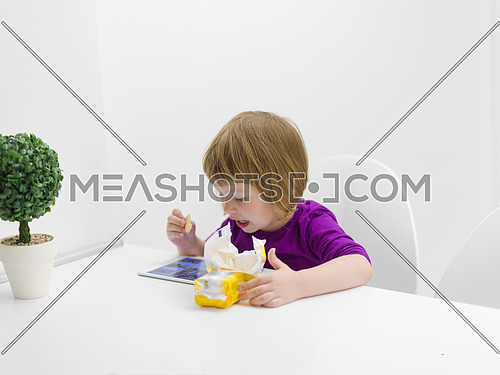 cute little girl eating a cookie while playing games on tablet computer at home