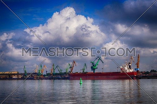 Cargo depot or wharf in a port with industrial cranes for loading and unloading cargo with a large tanker docked at the quay