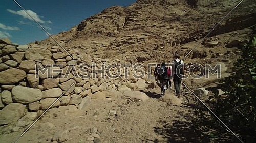 Reveal shot for group of tourists walking on big rocks with bedouin guide to explore Sinai Mountain for wadi Freij at day.
