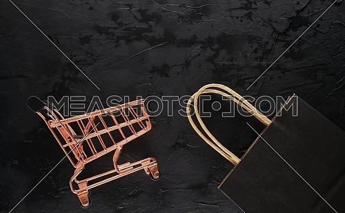 Shopping cart and black paper shopping bag on black grunge background with copy space for text, flat lay top view template. Black Friday sale, shopping concept
