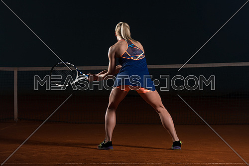 Female Tennis Player Reaching To Hit The Tennis Ball On Court - Back View