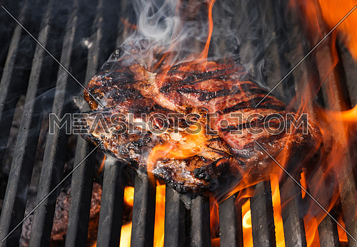 Close up searing and smoking ribeye beef steaks on open fire outdoor grill with cast iron metal grate, high angle view