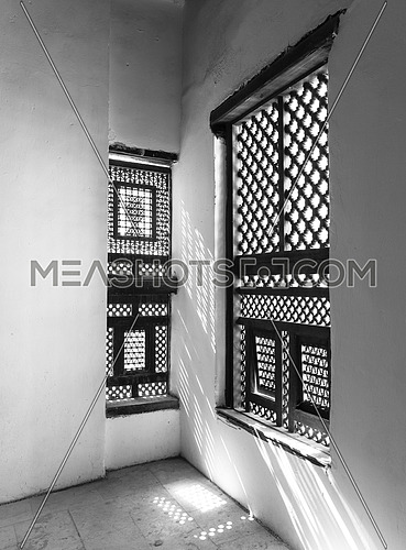 Black and white of corner of two Interleaved grunge wooden ornate windows - Mashrabiya - in stone wall at abandoned building