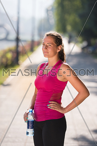 Athlete woman drinking water from a bottle after jogging in the city on a sunny day
