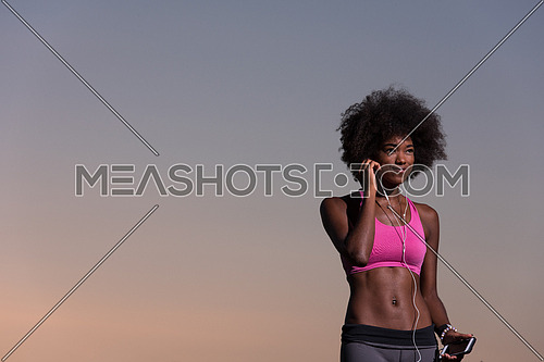 portrait of a young beautiful african american woman with headphones and mobile phone jogging in nature beautiful summer night