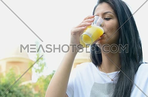 a young middle eastern woman drinking orange juice glass