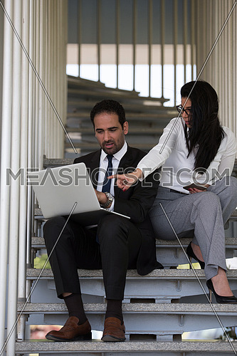 Business executives conducting business while sitting on steps in a corporate office using laptop,tablet and mobile phones