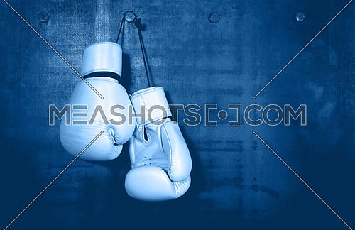 Close up pair of clasic white leather boxing gloves hanging over dark blue wall with copy space