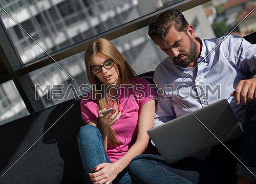 Young couple relaxing at luxury home using laptop computer reading in the living room on the sofa couch.