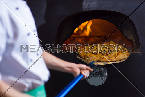 chef using special shovel to removing hot pizza from  stove where it was baked