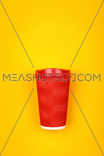 Close up one crimped disposable red paper takeaway coffee cup over vivid yellow background, flat lay, elevated top view, directly above