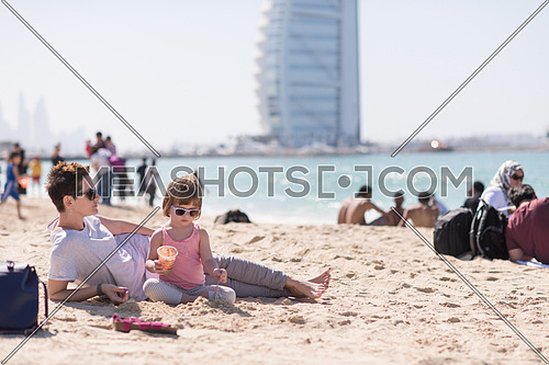 cool young mom and her little girl playing with a bucket full of sand wearing sunglasses and relaxing on the beach on a sunny day