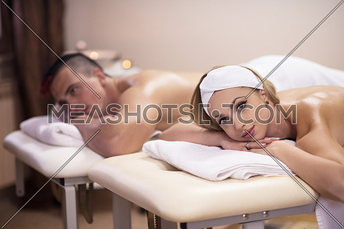 Portrait of relaxed beautiful young couple lying on massage table at spa center
