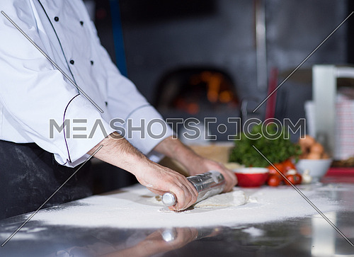 chef preparing dough for pizza rolling with rolling pin on sprinkled with flour table