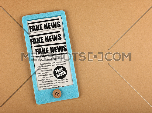 Close up felt craft blue smartphone with FAKE NEWS newspapers feed from screen over brown paper background, elevated top view, directly above