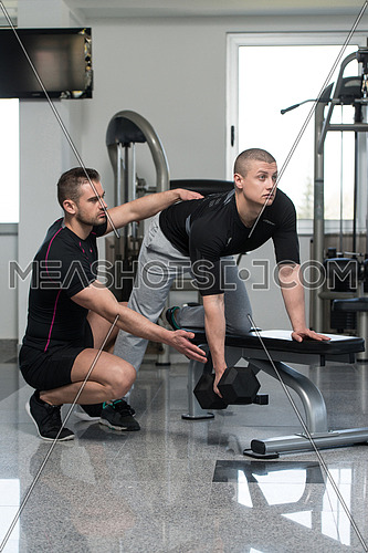 Personal Trainer Showing Young Man How To Train Back Exercise With Dumbbell In A Health And Fitness Concept