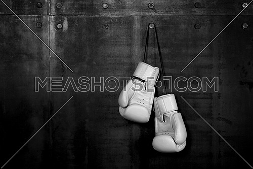 Close up pair of white leather boxing gloves hanging over black wall with copy space
