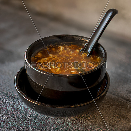Sour soup on black iron plate on grey stone slate background. side view,close up.