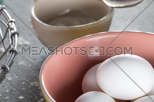 Eggs in a pink yellow bowl aside beige bowl with flour in it
