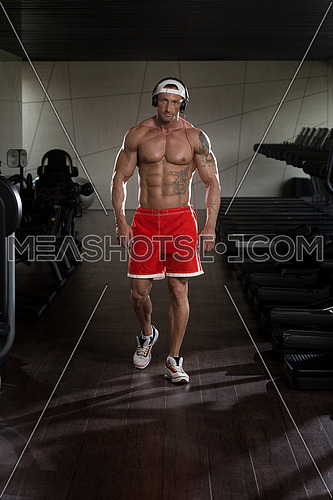 Muscular Mature Man Listening Music From His Mp3 Player In Modern Fitness Center