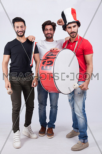 Three young men standing on a white background cheering with a drum