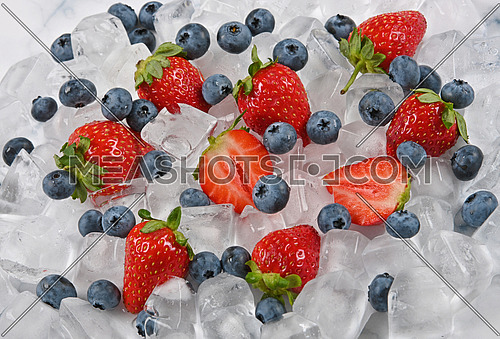 Close up fresh red ripe strawberries, blueberries and ice cubes on table, high angle view