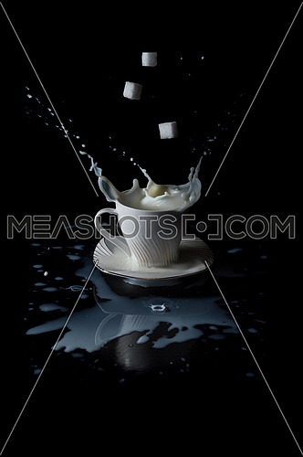 sugar cubes falling into cup of milk and splashing with black background.