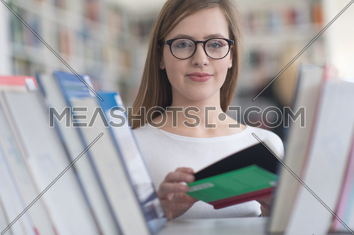 portrait of smart looking famale student girl  in collage school library,  selecting book to read from bookshelf