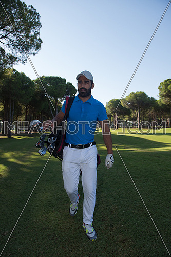 handsome middle eastern golf player carrying and bag  and walking at course on beautiful morning sunrise